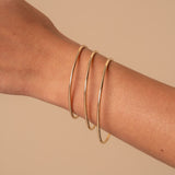 Gold bangles on a person's wrist against a beige background