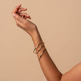 Arm wearing gold bangles on a beige background