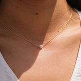 Gold necklace with a pearl pendant on a person wearing a white top.