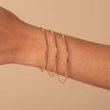 Gold bangles on a person's wrist against a beige background