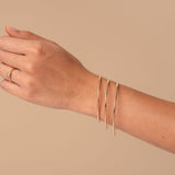 Hand wearing three gold bracelets on a beige background